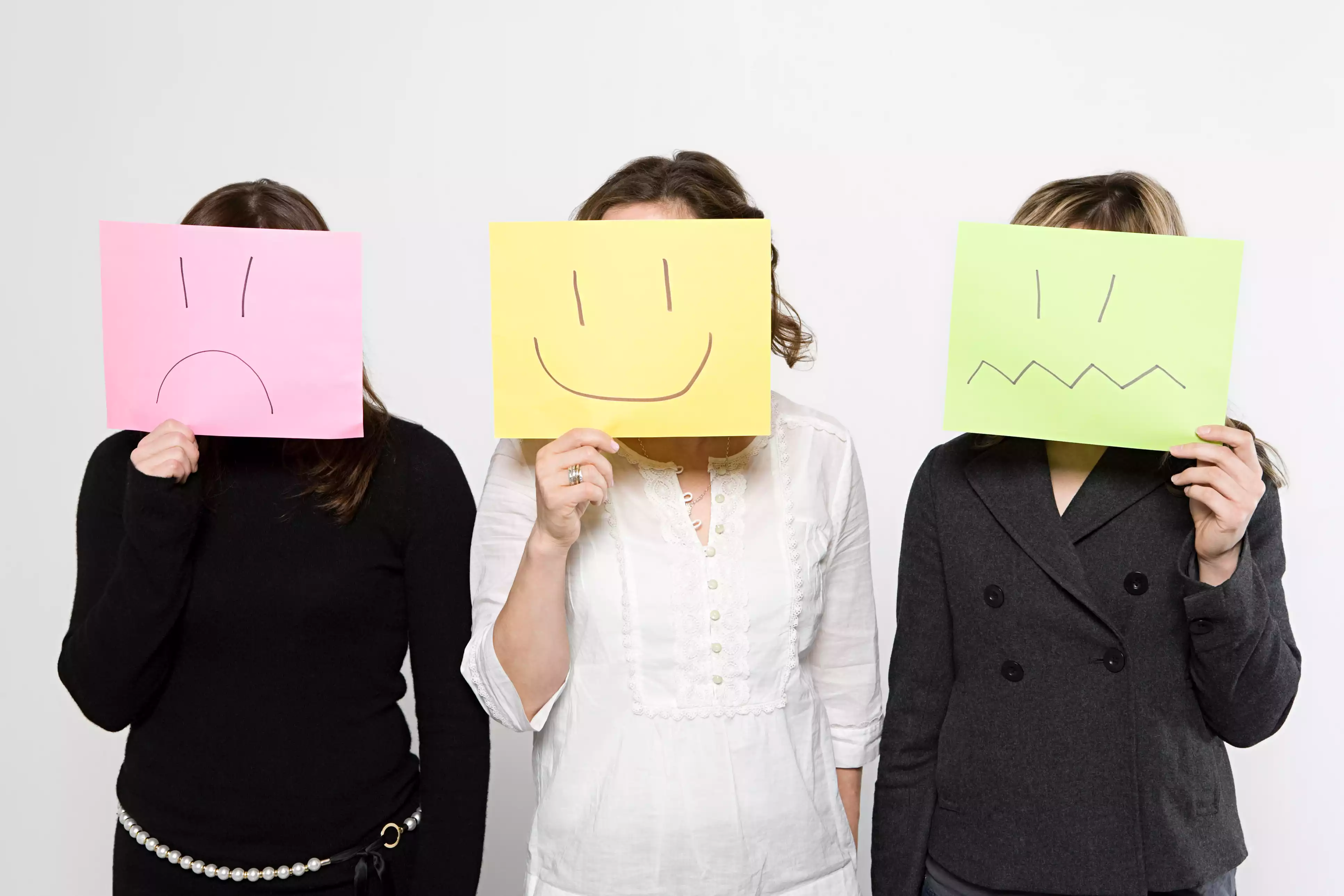 Three women holding papers over their faces with different expressions drawn on