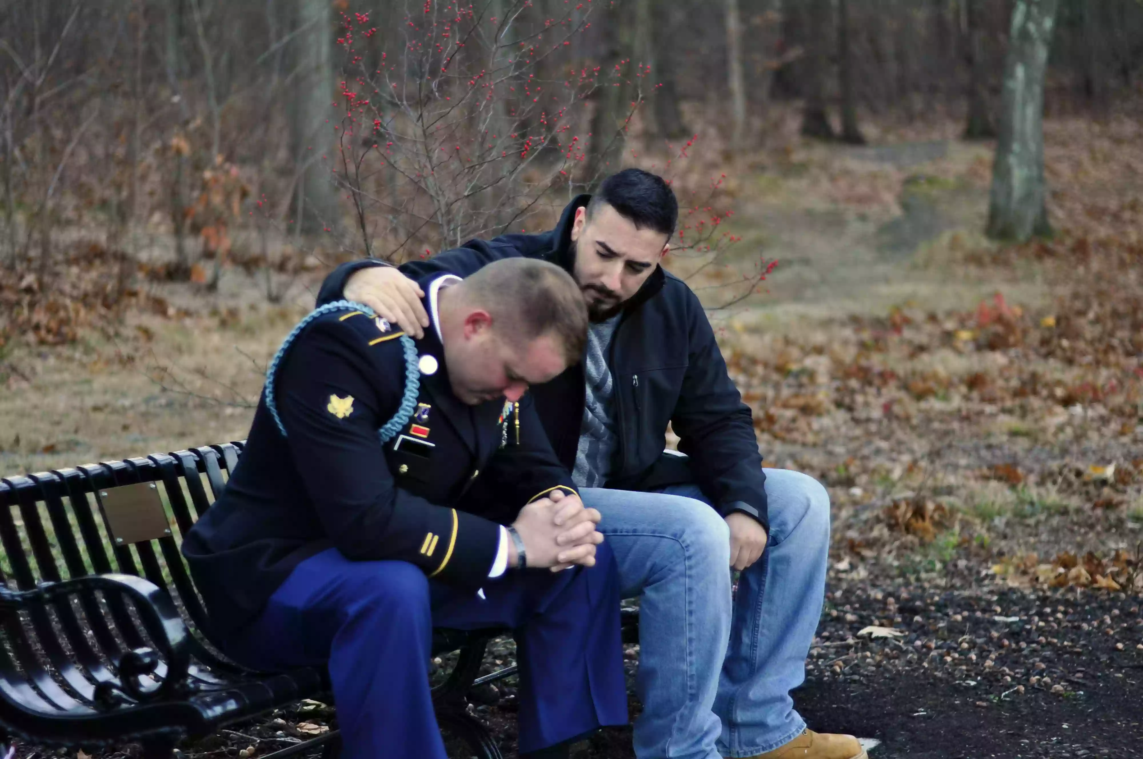 two men sitting on a park bench, one depressed and the other talking to and comforting him
